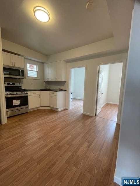 kitchen featuring appliances with stainless steel finishes, dark countertops, wood finished floors, a sink, and white cabinetry