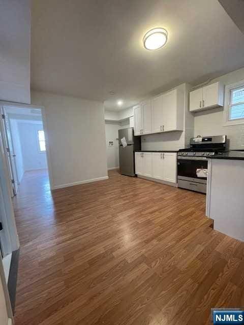 kitchen with stainless steel gas range, freestanding refrigerator, dark countertops, wood finished floors, and white cabinetry