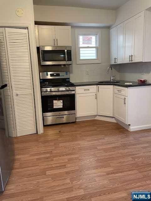 kitchen with stainless steel appliances, a sink, white cabinetry, light wood finished floors, and dark countertops