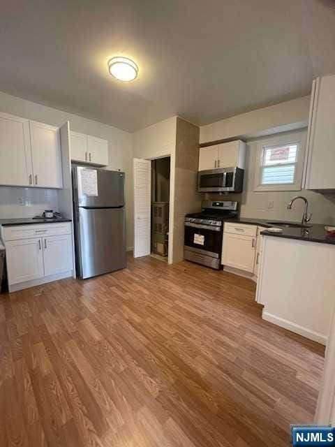 kitchen with stainless steel appliances, a sink, dark countertops, and wood finished floors