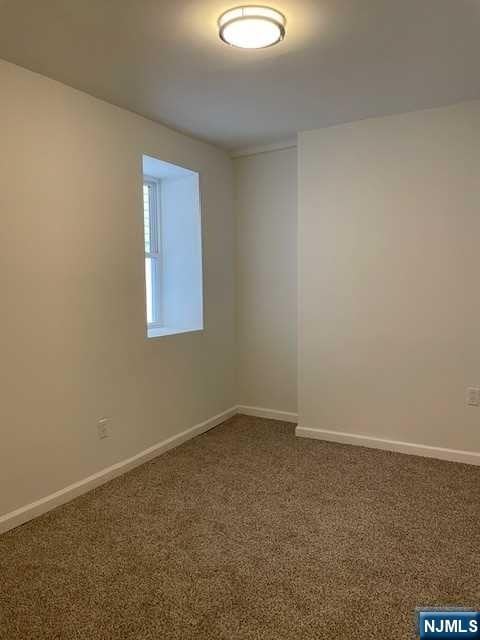 unfurnished room featuring dark carpet and baseboards