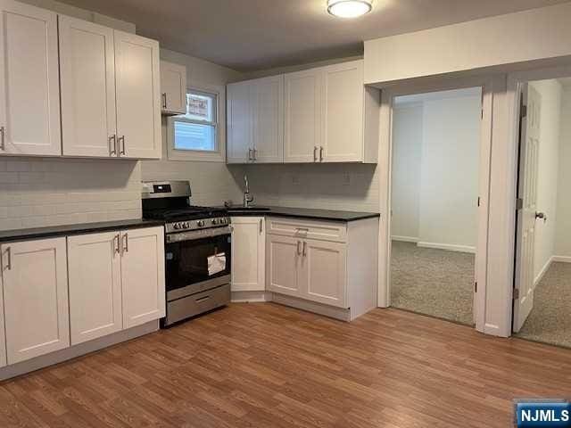 kitchen with stainless steel range with gas cooktop, dark countertops, wood finished floors, and white cabinets