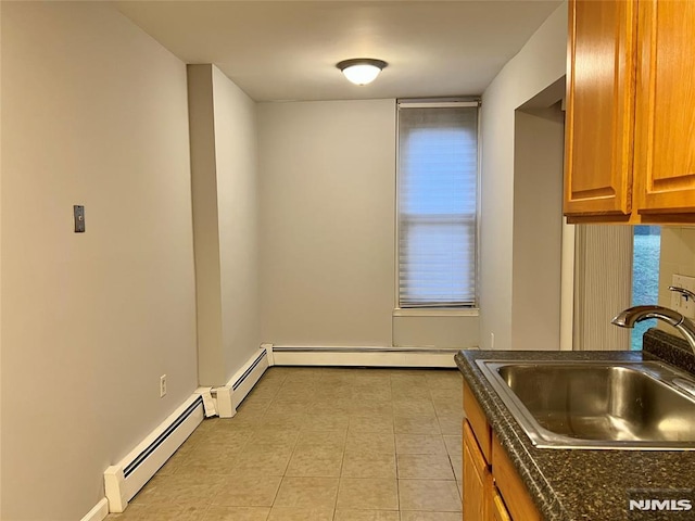 kitchen with a sink, dark countertops, brown cabinets, light tile patterned floors, and baseboard heating