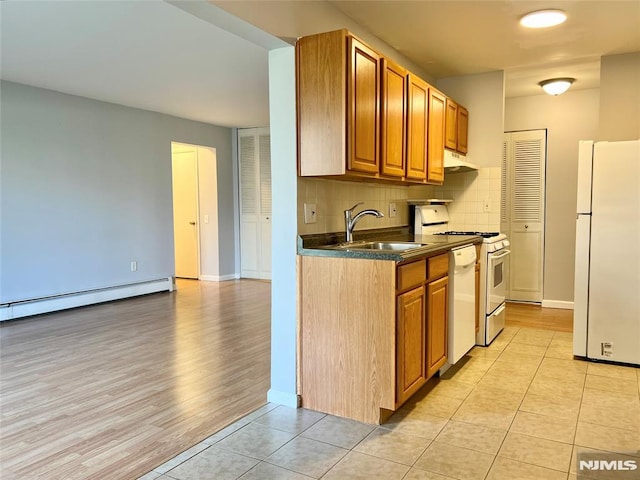 kitchen featuring white appliances, under cabinet range hood, a sink, dark countertops, and backsplash