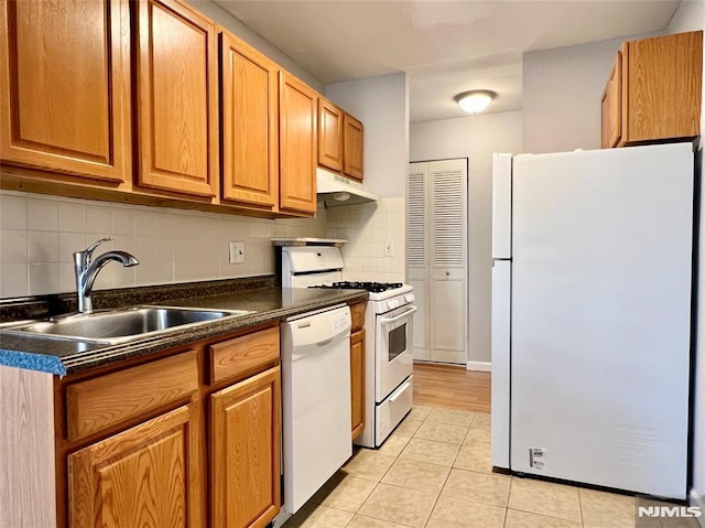kitchen featuring white appliances, a sink, under cabinet range hood, dark countertops, and decorative backsplash