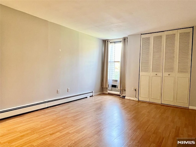 unfurnished bedroom with baseboard heating, wood finished floors, and baseboards