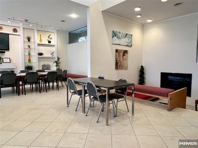 dining space with light tile patterned floors, rail lighting, crown molding, and built in features