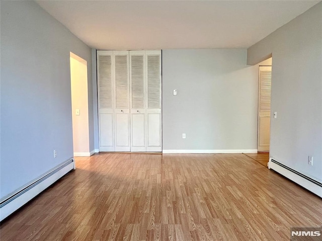 unfurnished bedroom featuring a baseboard heating unit, wood finished floors, baseboards, and a closet