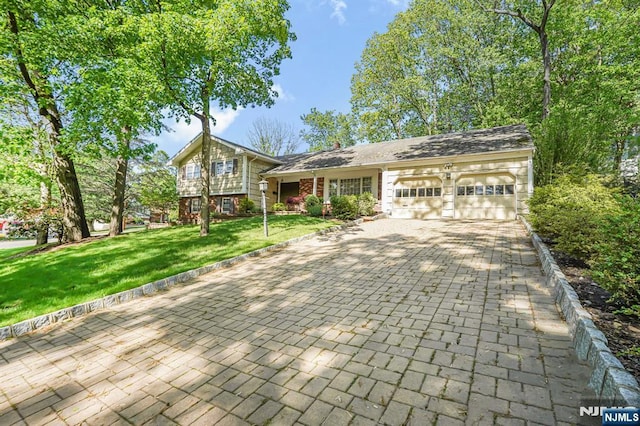 tri-level home with a garage, driveway, a front yard, and brick siding