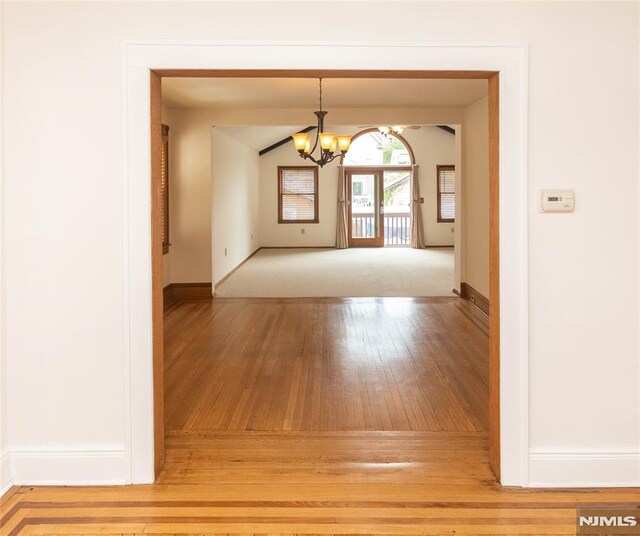 empty room featuring wood-type flooring, a chandelier, and baseboards