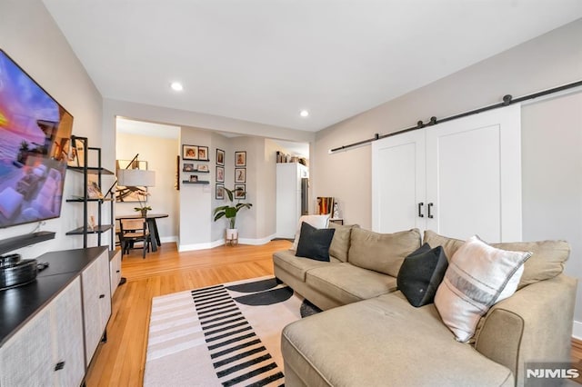 living room with a barn door, light wood finished floors, recessed lighting, and baseboards