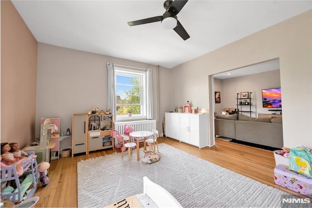 playroom with wood finished floors, a ceiling fan, and radiator heating unit