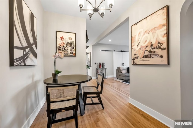 dining space with a barn door, arched walkways, light wood-style floors, recessed lighting, and a chandelier