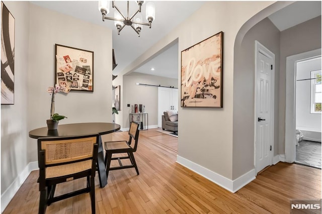 dining area with a barn door, light wood-style floors, arched walkways, a chandelier, and recessed lighting
