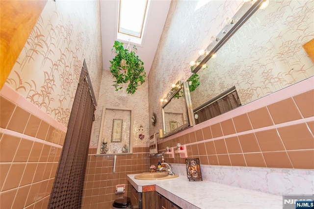 bathroom featuring wallpapered walls, a wainscoted wall, vanity, and tile walls