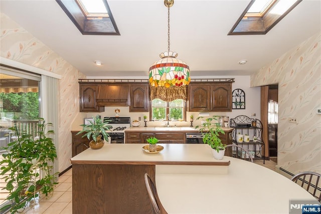 kitchen featuring a skylight, gas stove, wallpapered walls, light countertops, and light tile patterned flooring
