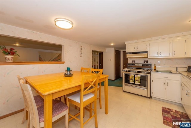 kitchen with gas range, under cabinet range hood, white cabinetry, light flooring, and light countertops