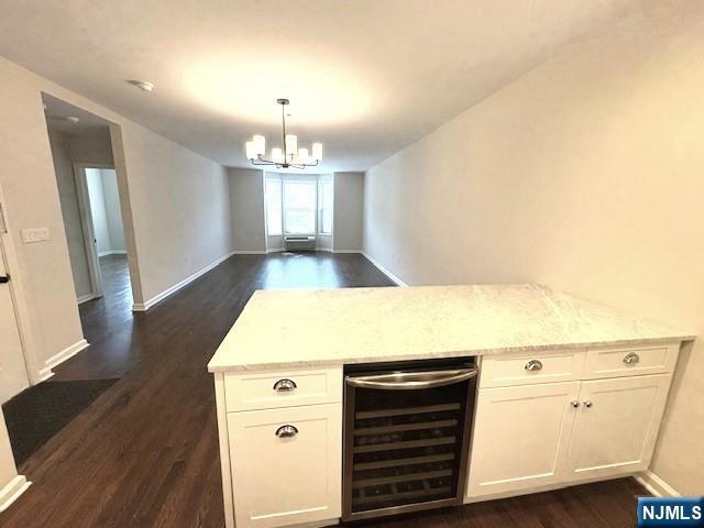 unfurnished dining area featuring beverage cooler, dark wood-style flooring, a chandelier, and baseboards