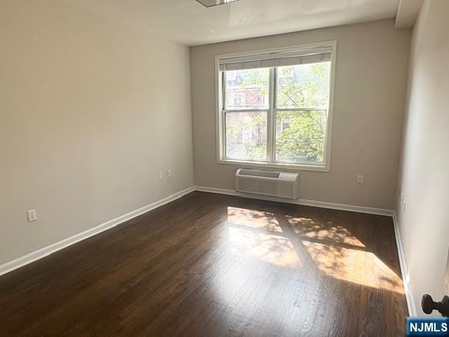 spare room featuring a wall unit AC, dark wood-style floors, and baseboards