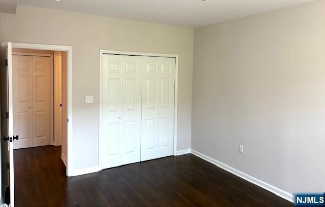 unfurnished bedroom with baseboards, dark wood-type flooring, and a closet