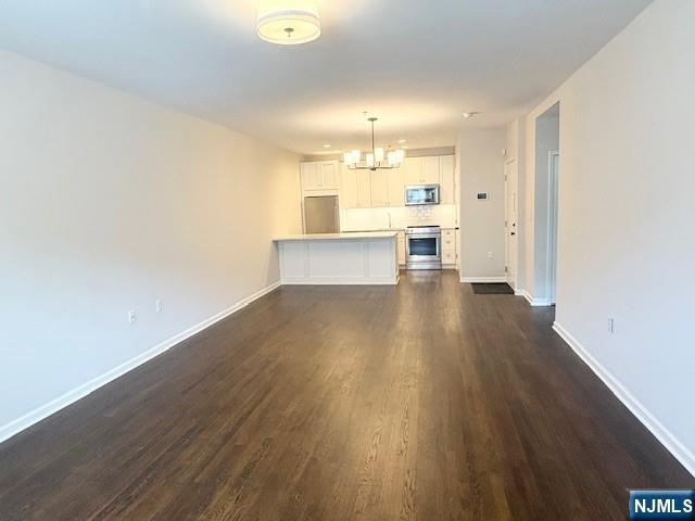 unfurnished living room featuring a chandelier, dark wood-style floors, and baseboards