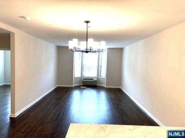 unfurnished dining area with a chandelier, dark wood finished floors, baseboards, and a wall unit AC