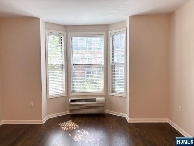 empty room featuring a wall unit AC, baseboards, and wood finished floors