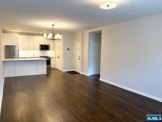 kitchen with appliances with stainless steel finishes, a chandelier, tasteful backsplash, baseboards, and white cabinetry