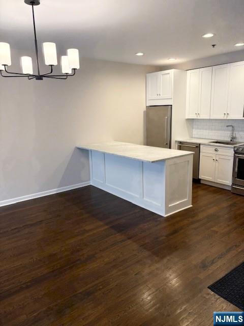 kitchen with appliances with stainless steel finishes, a sink, a chandelier, white cabinetry, and light countertops
