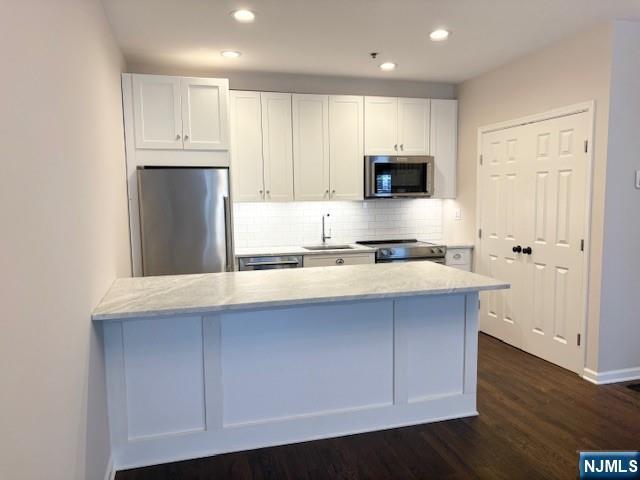 kitchen featuring stainless steel appliances, a sink, white cabinets, tasteful backsplash, and dark wood-style floors