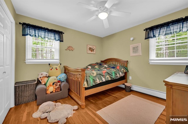 bedroom featuring a baseboard heating unit, a closet, wood finished floors, a ceiling fan, and baseboards