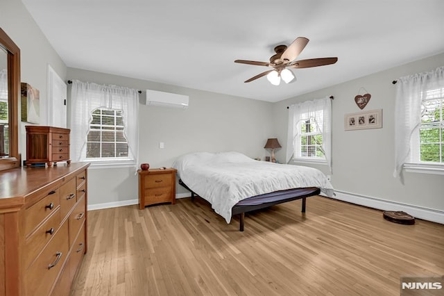 bedroom with a wall mounted air conditioner, multiple windows, light wood-type flooring, and baseboards