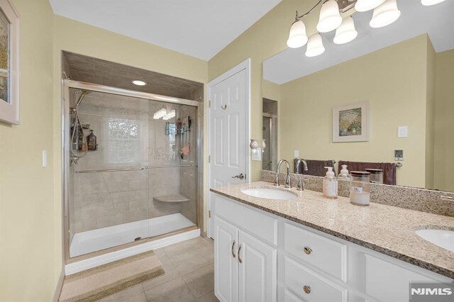 bathroom featuring a shower stall, double vanity, and tile patterned flooring