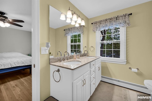 ensuite bathroom featuring baseboard heating, double vanity, and a ceiling fan