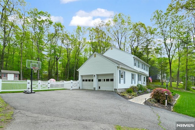 view of property exterior featuring a gate, asphalt driveway, an attached garage, and fence