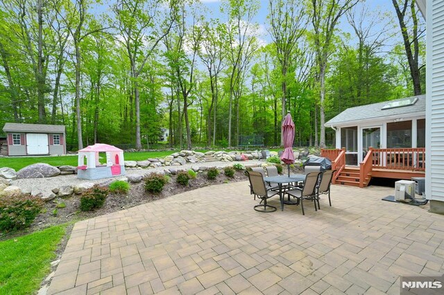 view of patio with a sunroom, outdoor dining space, a deck, an outbuilding, and a storage shed