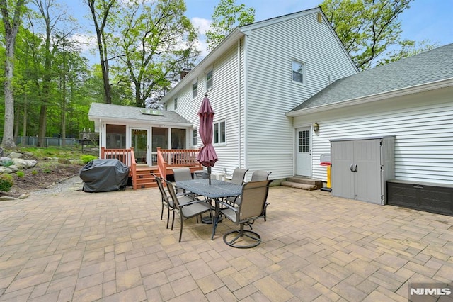 view of patio / terrace featuring a grill, a sunroom, a deck, outdoor dining area, and entry steps