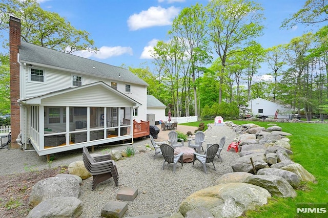 back of house featuring an outdoor fire pit, a sunroom, a chimney, fence, and a deck