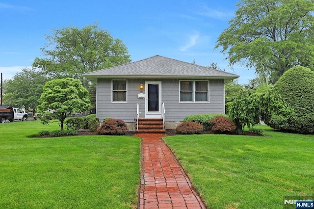 bungalow-style home with a front yard, entry steps, and a shingled roof