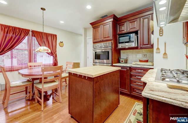 kitchen with appliances with stainless steel finishes, light wood-style floors, hanging light fixtures, a kitchen island, and backsplash