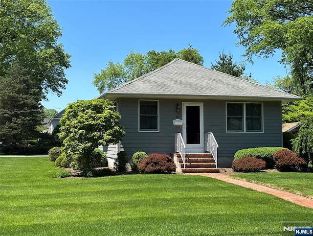 bungalow-style house with entry steps, a front lawn, and roof with shingles