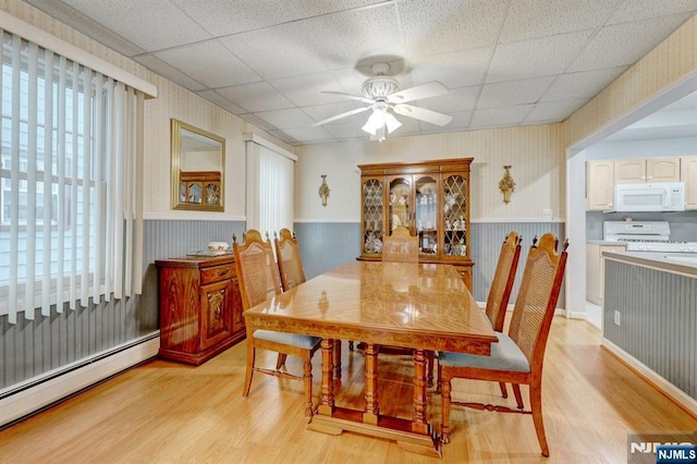 dining room with a baseboard radiator, light wood finished floors, wallpapered walls, a wainscoted wall, and a ceiling fan