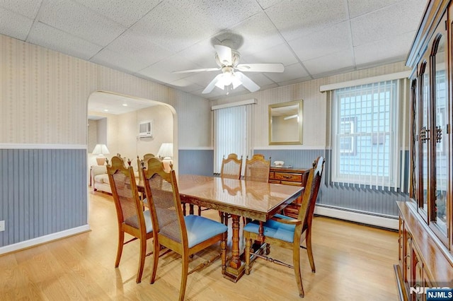 dining room featuring wallpapered walls, a baseboard radiator, light wood finished floors, wainscoting, and arched walkways