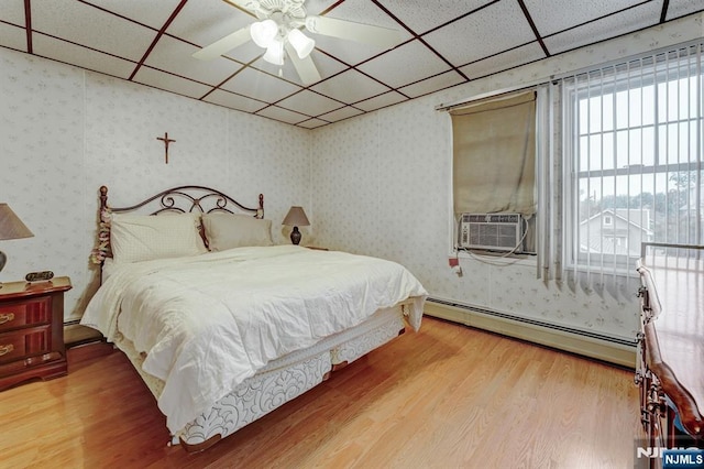 bedroom featuring a baseboard heating unit, a paneled ceiling, wallpapered walls, wood finished floors, and cooling unit