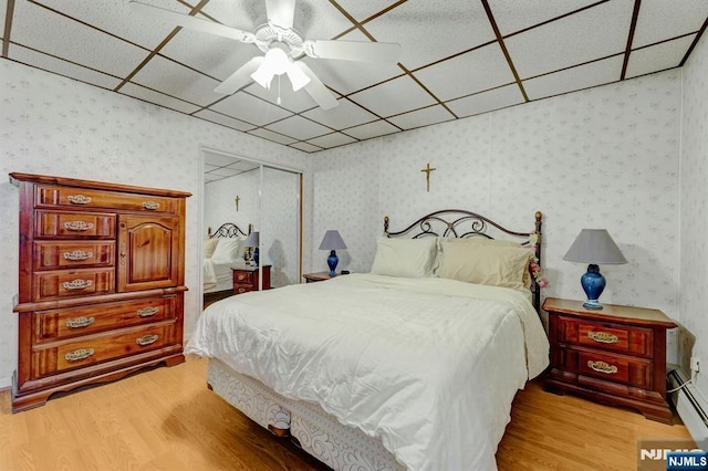 bedroom with wood finished floors, wallpapered walls, a paneled ceiling, a closet, and a baseboard radiator