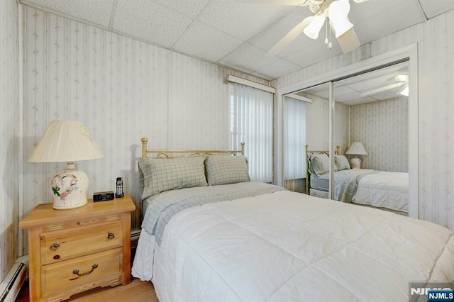 bedroom featuring wallpapered walls, a baseboard heating unit, wood finished floors, a closet, and a ceiling fan