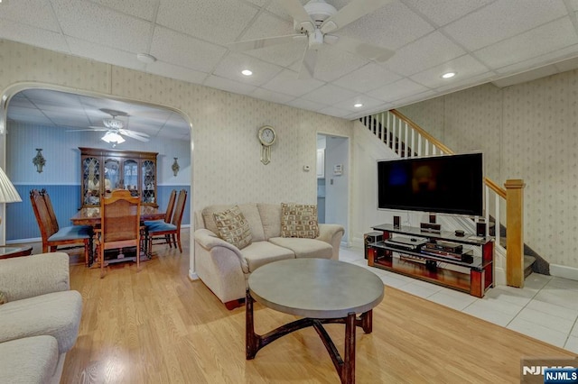 living room featuring a ceiling fan, wallpapered walls, stairs, wood finished floors, and wainscoting