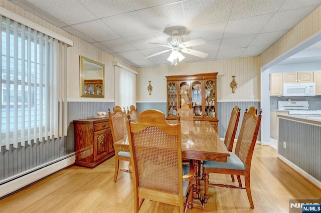dining room with a baseboard radiator, wallpapered walls, light wood-type flooring, a wainscoted wall, and a ceiling fan