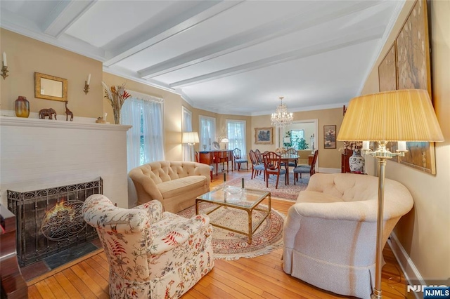 living area with a chandelier, light wood-type flooring, beamed ceiling, a lit fireplace, and baseboards
