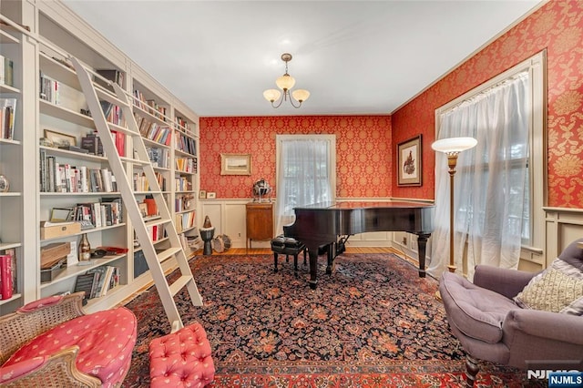 living area featuring wallpapered walls, wainscoting, a chandelier, wood finished floors, and crown molding